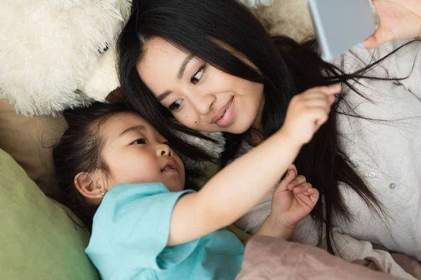 Asiática Chica Apuntando Smartphone Cerca Madre Suave Juguete Cama — Foto de Stock