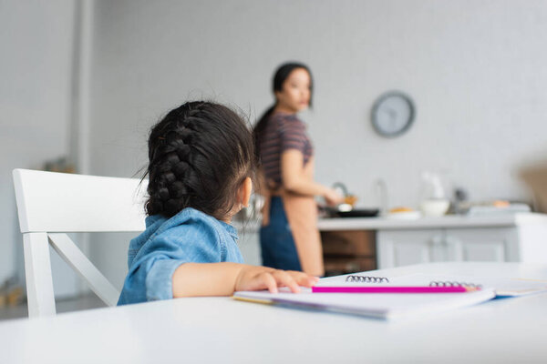 Kid sitting near pencil and paper in kitchen 