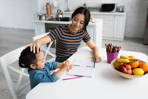 Sorridente Madre Toccando Figlia Asiatica Vicino Matite Colore Frutta Cucina — Foto Stock