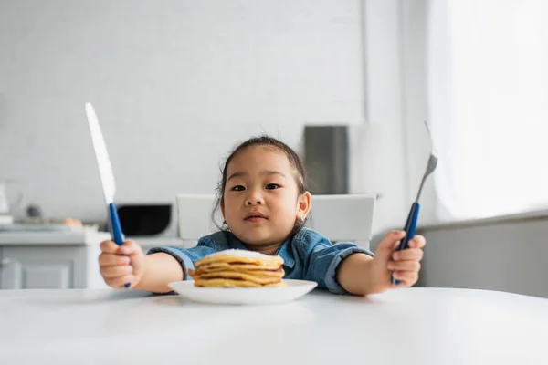 Азиатский Ребенок Держит Столовые Приборы Рядом Вкусными Блинами Дома — стоковое фото