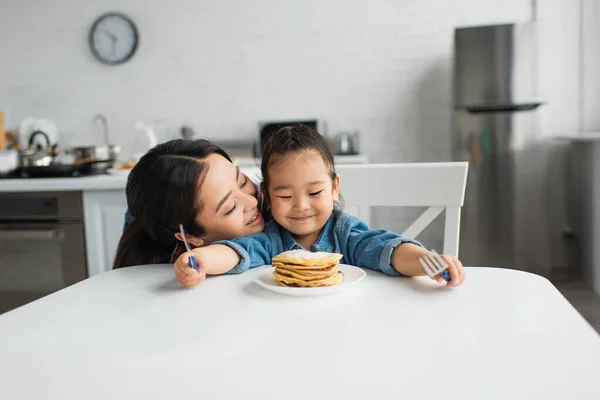 Asiática Mujer Besos Sonriente Hija Cerca Panqueques Casa — Foto de Stock