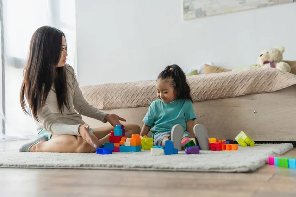 Lächelndes Asiatisches Mädchen Sitzt Neben Mutter Und Zeigt Auf Bauklötze — Stockfoto