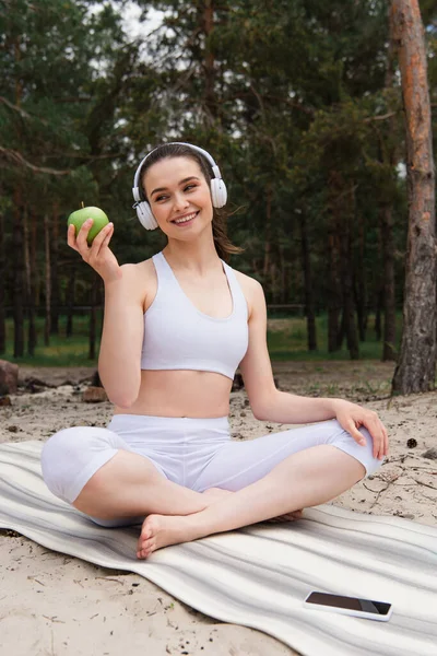 快乐的女人 头戴耳机 一边在树林里听音乐 一边拿着苹果 — 图库照片
