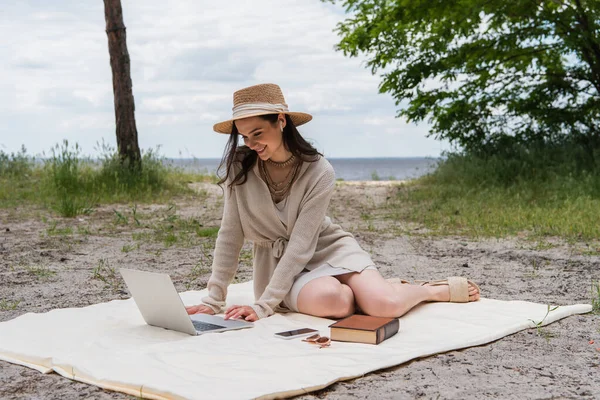 Felice Donna Cappello Paglia Auricolari Utilizzando Computer Portatile Mentre Seduto — Foto Stock