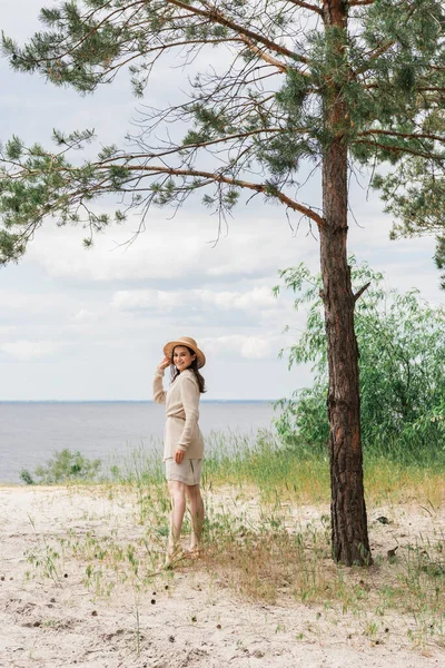 Full Length Smiling Young Woman Adjusting Straw Hat Standing Woods — Stock Photo, Image