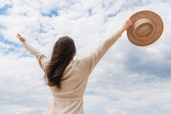 back view of young woman standing with outstretched hands against cloudy sky