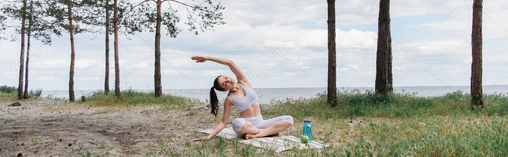 young woman sitting with crossed legs and stretching in forest, banner