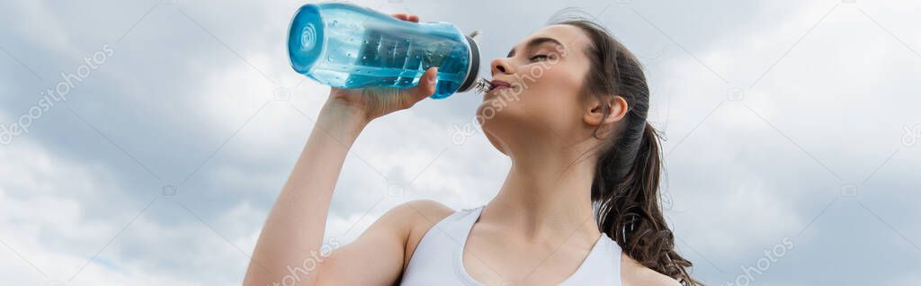 low angle view of young woman in crop top drinking water against blue sky with clouds, banner