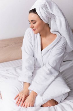 happy woman in towel on head and bathrobe sitting in bedroom  clipart