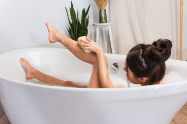 Saçları topuzlu genç bir kadın banyo yaparken banyo lifi ile banyo yapıyor. 