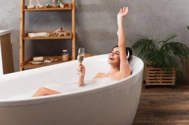 Kulaklıklı mutlu kadın müzik dinliyor ve banyo yaparken bir bardak şampanya tutuyor. 