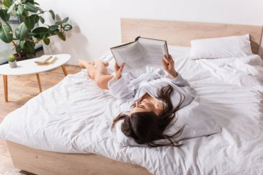 Bornozlu neşeli kadın yatakta uzanıyor ve evde kitap okuyor.