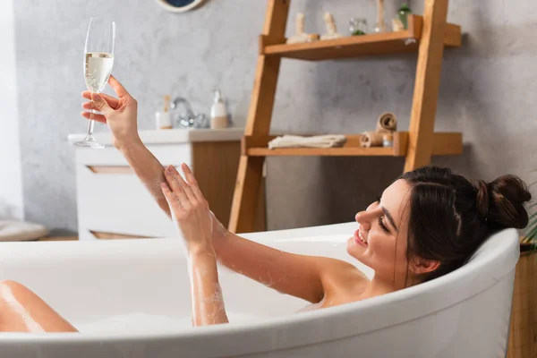 快乐的女人在浴缸里洗澡的时候举着一杯香槟 — 图库照片