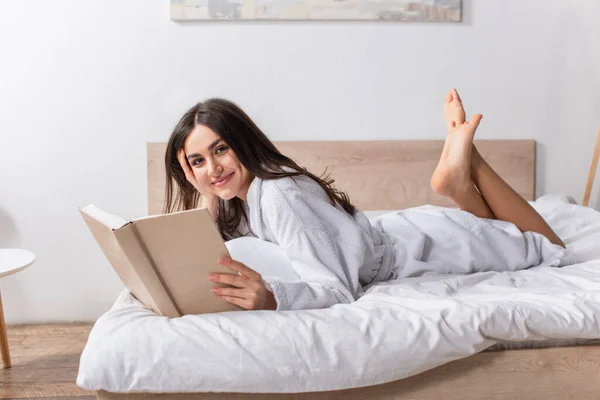 Young Joyful Woman Bathrobe Lying Bed Holding Book — Stock Photo, Image