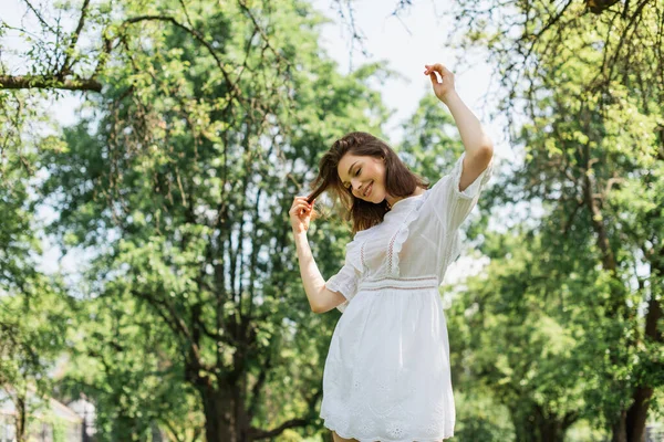 Giovane Donna Sorridente Mentre Tocca Capelli Nel Parco — Foto Stock