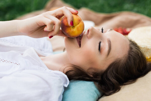 Smiling woman holding peach while lying on blanket in park 