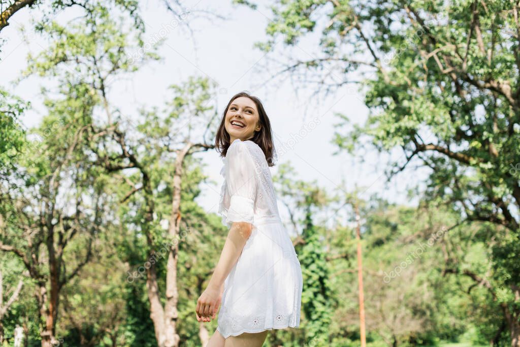 Happy woman in white dress standing in summer park 