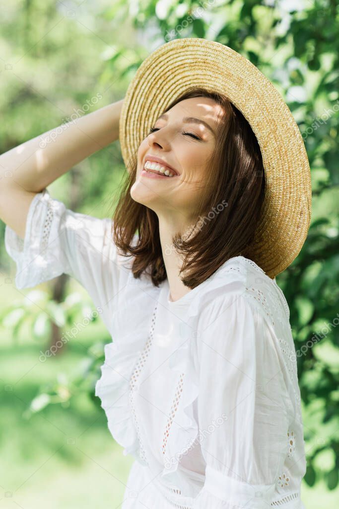 Happy woman in white dress holding sun hat in park 