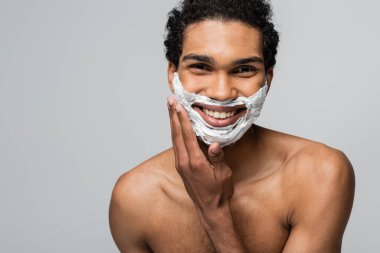 shirtless and happy african american man applying shaving foam on face isolated on grey clipart
