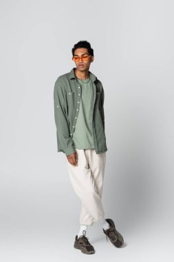 Gri arka planda turuncu gözlüklü, şık giyinen Afro-Amerikan bir adam.