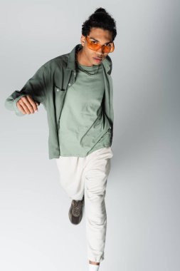 Gri arka planda yürüyen gözlüklü şık Afrikalı Amerikalı adamın yüksek açılı görüntüsü