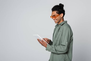 Gülümseyen ve modaya uyan Afrikalı Amerikalı adam gri tablet kullanıyor.