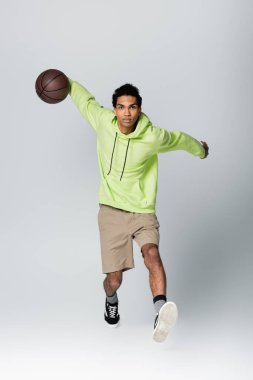 Gri arka planda basketbol oynayan Afro-Amerikan erkeğinin tam boy görüşü