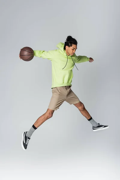 African American Guy Hoodie Shorts Sneakers Jumping Basketball Grey Background — Stock Photo, Image
