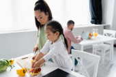 asian mother and child preparing salad near blurred man at home