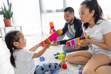 Asyalı ebeveynler yeni yürümeye başlayan kızlarıyla yapı taşı oynuyorlar 