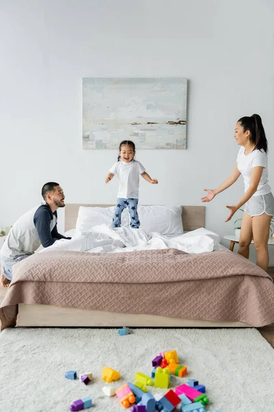 快乐的亚洲父母看着蹒跚学步的女儿在床上跳 — 图库照片