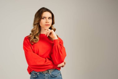 Kırmızı eşofmanlı düşünceli bir kadın gözlerini kaçırıyor ve gri üzerinde yalnız olduğunu düşünüyor.