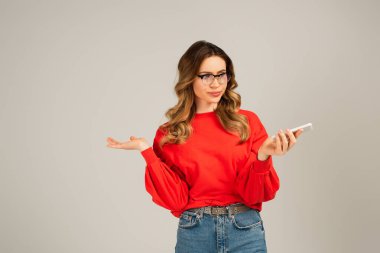 Gri renkte izole edilmiş akıllı telefon kullanan gözlüklü tatmin olmamış bir kadın.