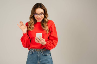 Gözlüklü mutlu kadın, gri telefondan görüntülü arama yapıyor.