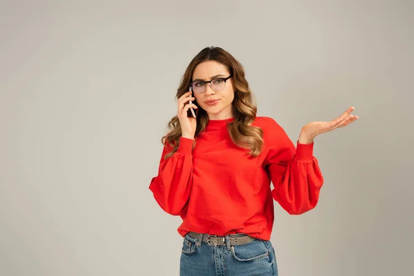 Confused Woman Eyeglasses Talking Smartphone While Gesturing Isolated Grey — Stock Photo, Image