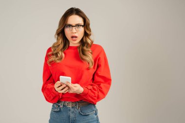 Gözlüklü ve kırmızı eşofmanlı kadının elinde gri renkli akıllı telefon vardı.