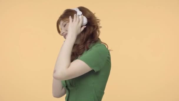 Glücklich Rothaarige Teenager Mädchen Mit Kopfhörern Tanzen Isoliert Auf Gelb — Stockvideo