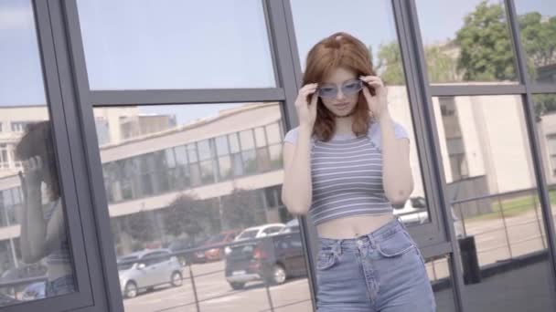 Szczęśliwy Ruda Nastolatek Dziewczyna Zdejmując Okulary Przeciwsłoneczne Pobliżu Budynku — Wideo stockowe