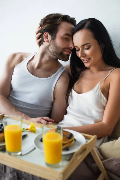 幸せな女性抱擁ひげを生やしたボーイフレンドと朝食トレイを見て — ストック写真