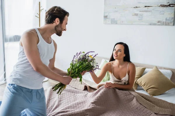 Alegre Hombre Celebración Ramo Flores Cerca Novia Acostado Cama — Foto de Stock