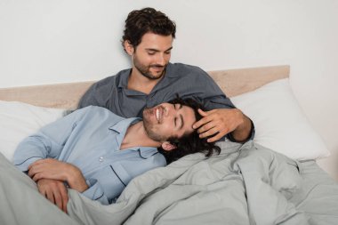 Eşcinsel adam yatakta erkek arkadaşının saçını okşuyor.