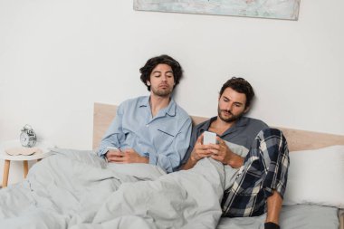 Erkek arkadaşı yatakta sohbet ederken cep telefonuna bakan bir adam.