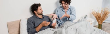 Canı sıkkın bir adam, erkek arkadaşının akıllı telefon ve afişte konuşmasına bakıyor.