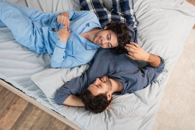 top view of cheerful gay couple in pajamas resting on bed clipart