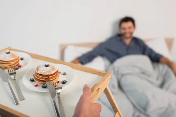 Hombre Sosteniendo Bandeja Desayuno Con Panqueques Cerca Borrosa Novio Cama — Foto de Stock