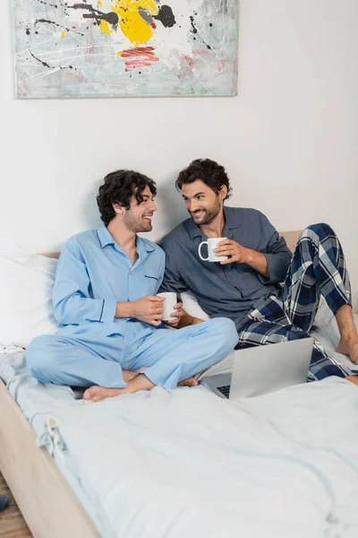 Feliz Gay Casal Segurando Copos Chá Perto Laptop Cama — Fotografia de Stock