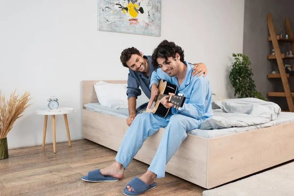 Sonriente Gay Hombre Jugando Acústica Guitarra Cerca Feliz Novio Cama — Foto de Stock