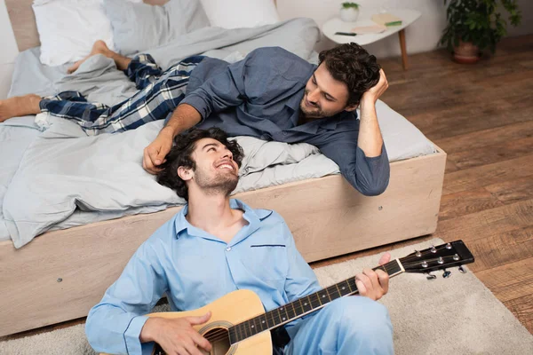 Sorridente Gay Uomo Giocare Acustica Chitarra Vicino Barbuto Fidanzato Letto — Foto Stock