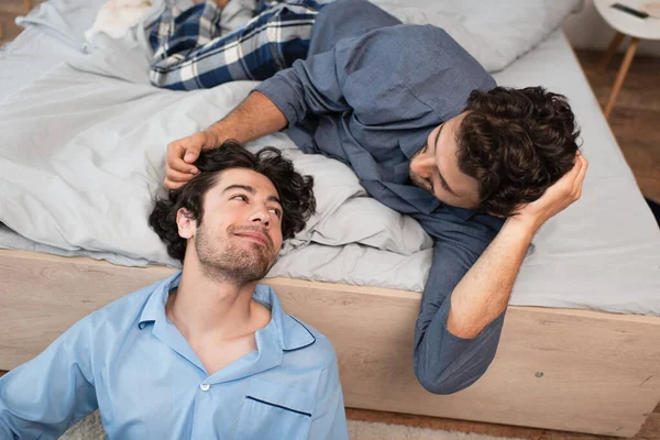 caring man stroking hair of boyfriend in bedroom