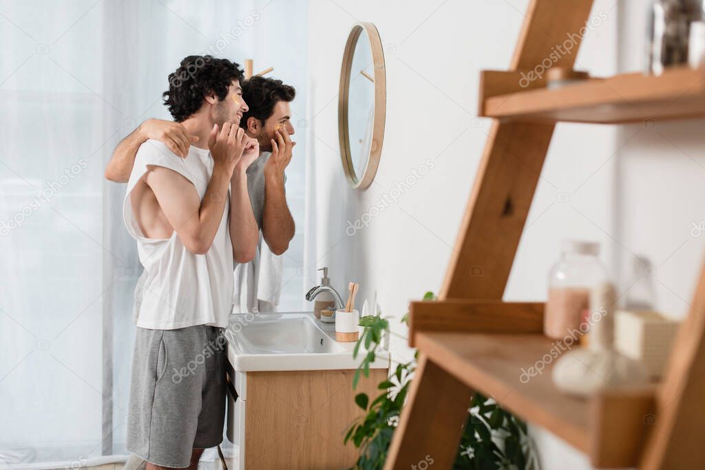 cheerful gay couple applying eye patches in bathroom